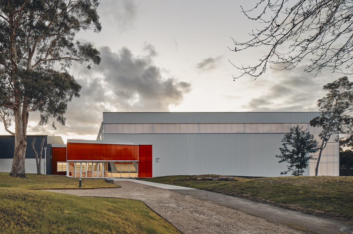 Cranbourne Secondary College - photo of a gymnasium from an outdoor pathway surrounded by grass and trees