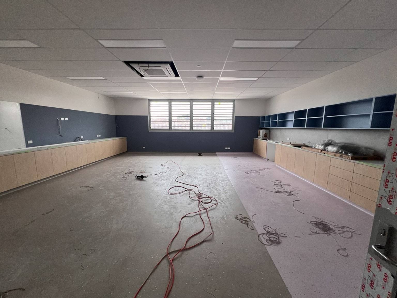 New classroom constructed with a blue, white, timber, and pink colour palette. Electrical cabling strewn across the floor. 