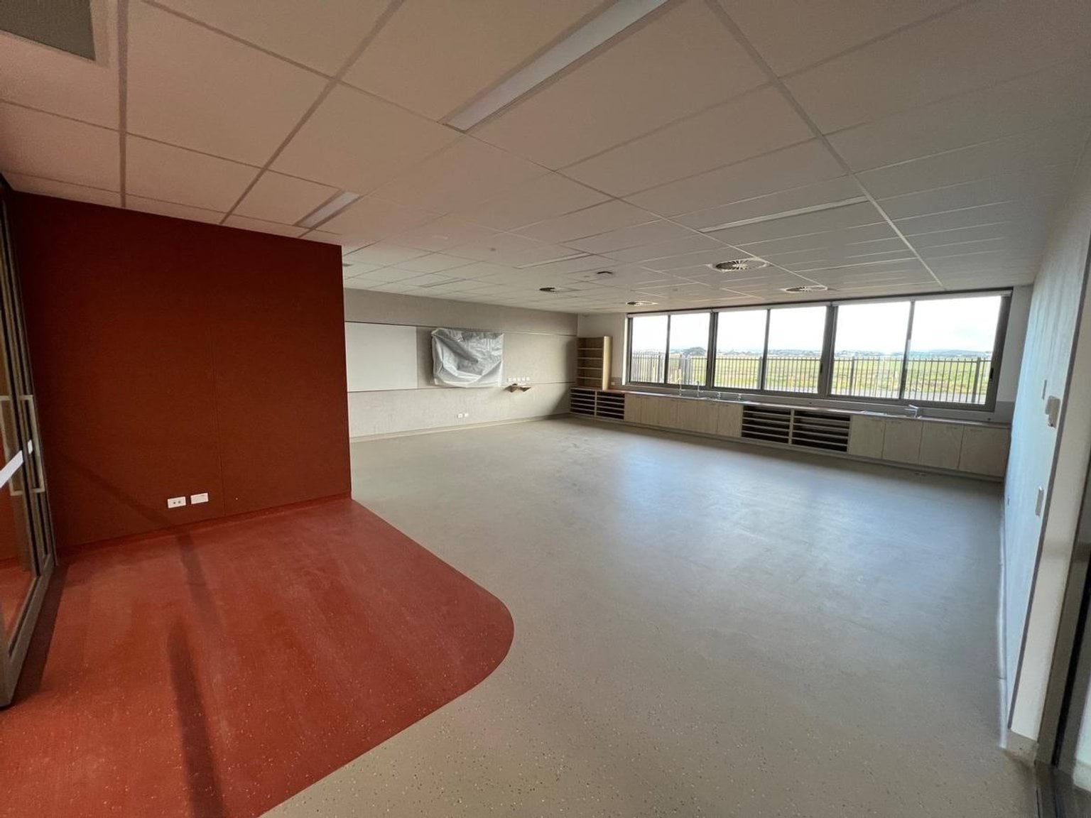 Red zoned area with floor and feature wall demarcating classroom space. A bay of windows let natural light in from the rear of the classroom. The classroom is yet to be furnished. 