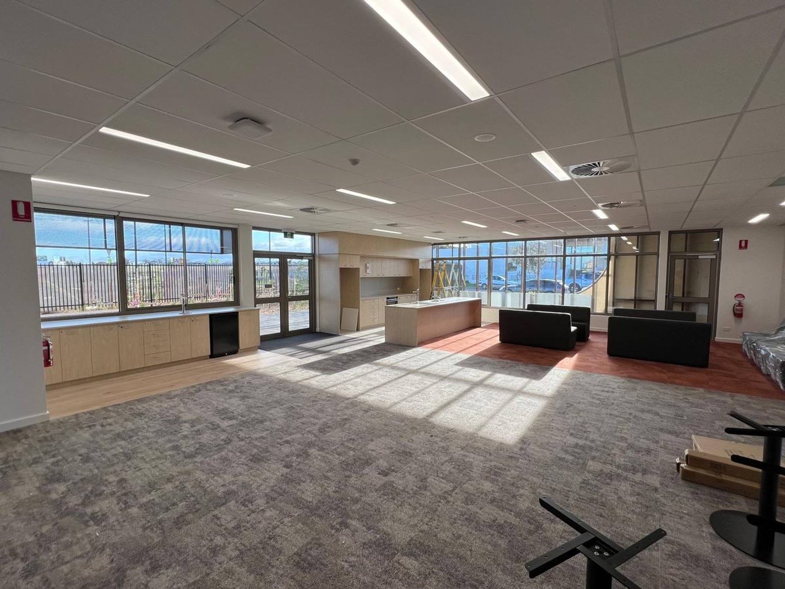 Light streaming through large windows at rear of common area that has some couches and upside down table on the carpet