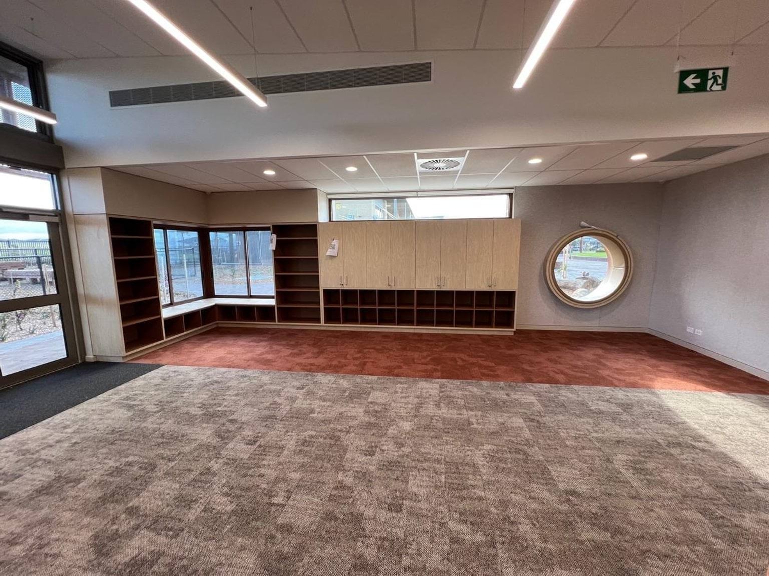 Red and tan coloured carpet in open unfurnished space. Open timber pigeon holes between windows of different shapes and sizes (rectangular, circular). 