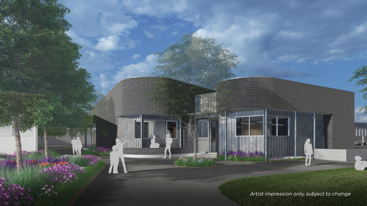 Two circular grey brick buildings are connected by a colour bond panels and below this the entrance door. Two paths fork to allow access to both buildings. 