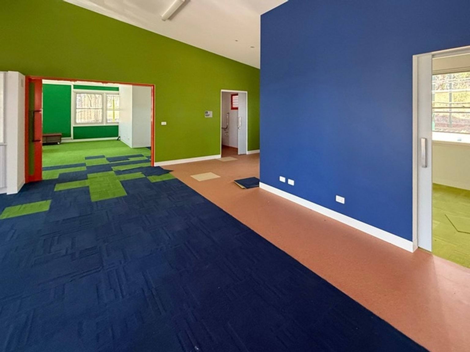 Indoor photo of a school building. It is a carpeted area with green and blue walls. There are doorways opening to other rooms.