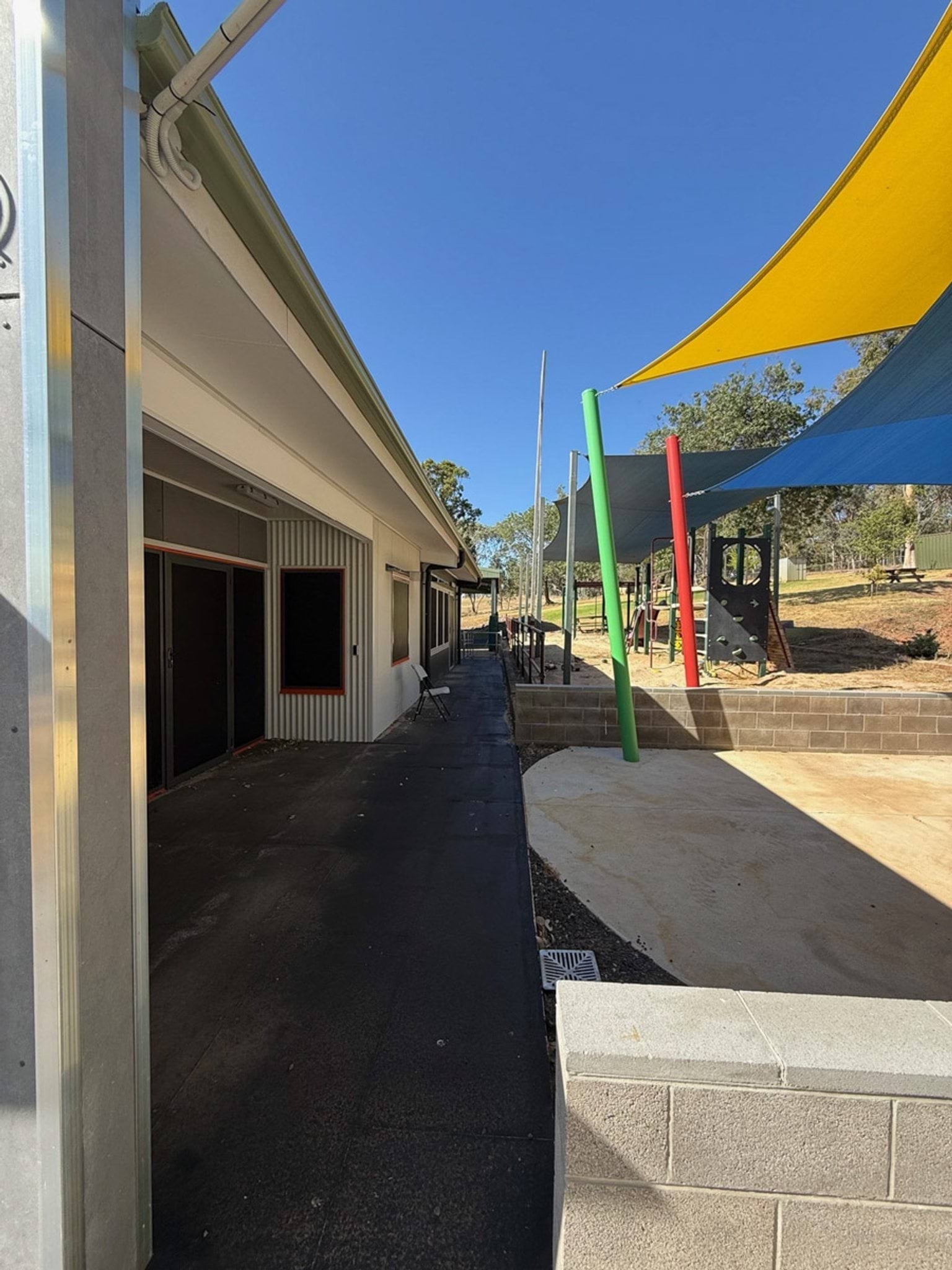 Outdoor photo of Currawa Primary School showing a pathway which runs between a school building and an undercover play area.
