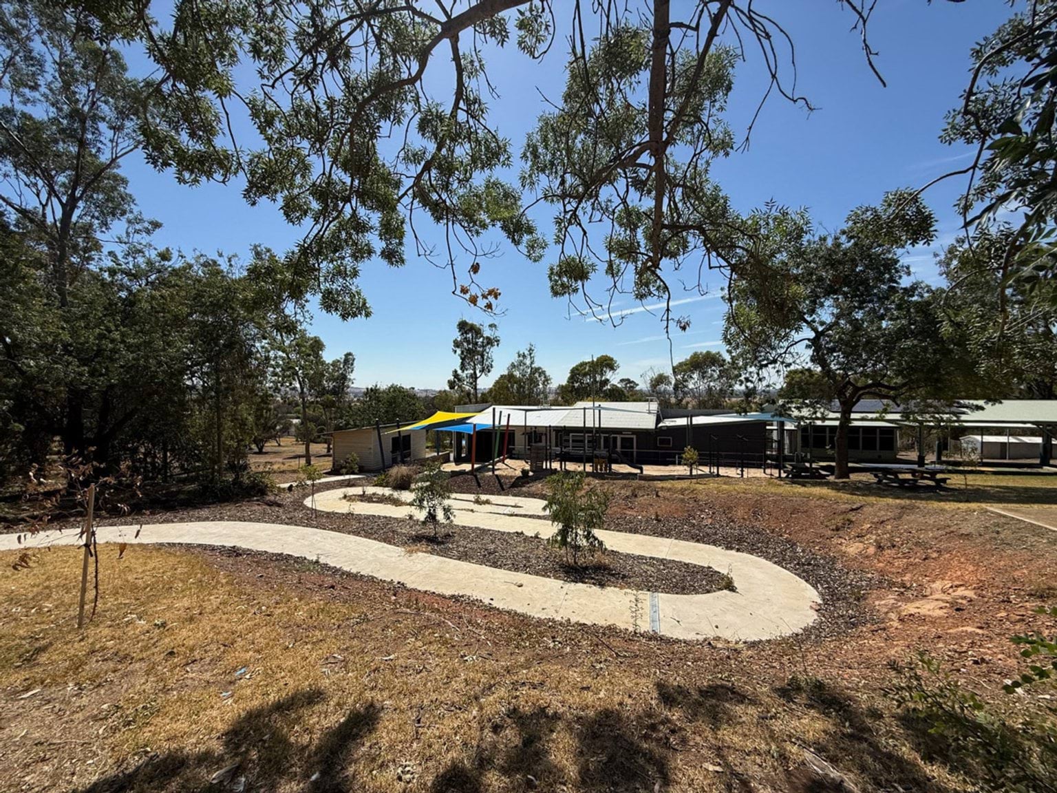 Outdoor photo of a path leading to a school building. It is surrounded by shrubs and trees.