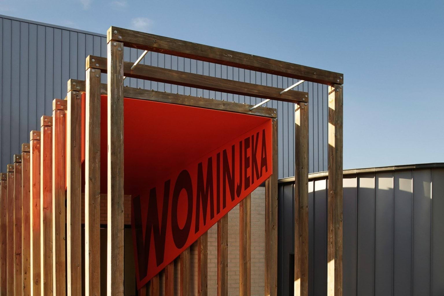 An entry way built using wooden square arches. There is a red banner with the word 'Wominjeka' in big letters, which means 'welcome' in the Woiwurrung language.