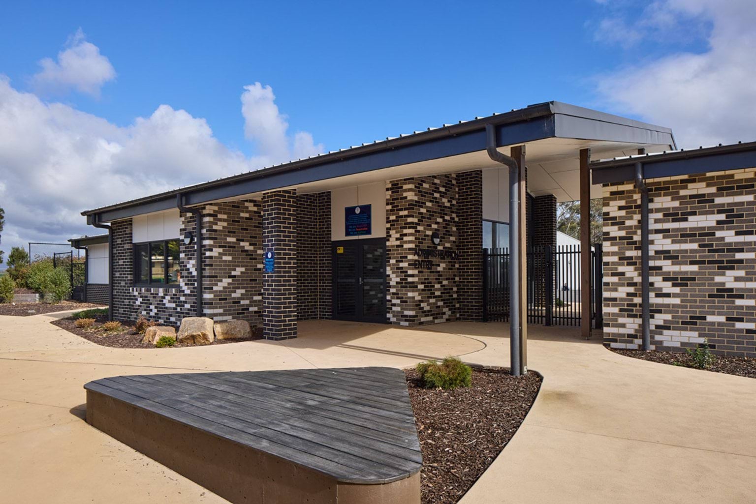 Outdoor photo of entrance to Hazelwood North Primary School. It has a modern design with brown, white, and black bricks, paths, and a nearby seating area.