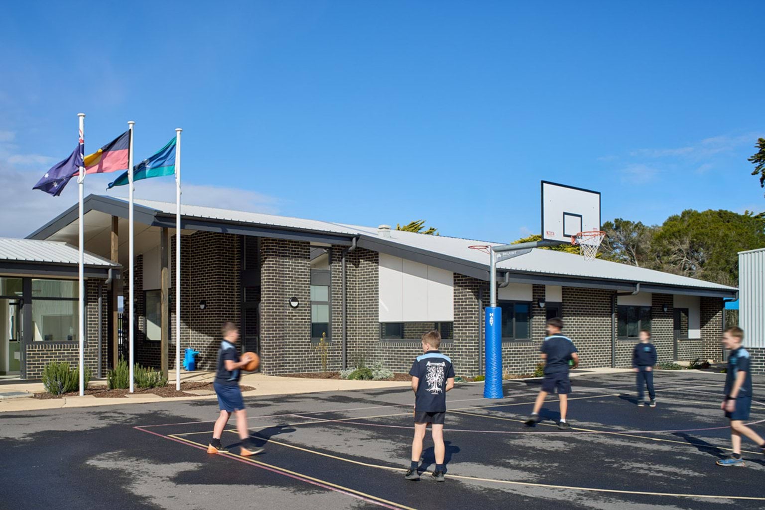 Outdoor photo of basketball court. There are five children in school uniforms playing basketball.