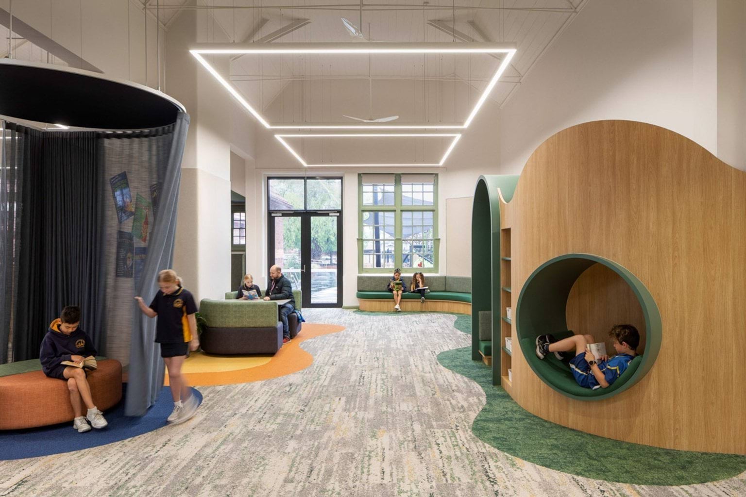 Inside Moonee Ponds West Primary School. On the left are couches, one with a curtain that can be closed around it. On the right is a wall with recessed sections to sit in. On the far back wall is a bench seat wrapping around the wall and a door leading to outside.