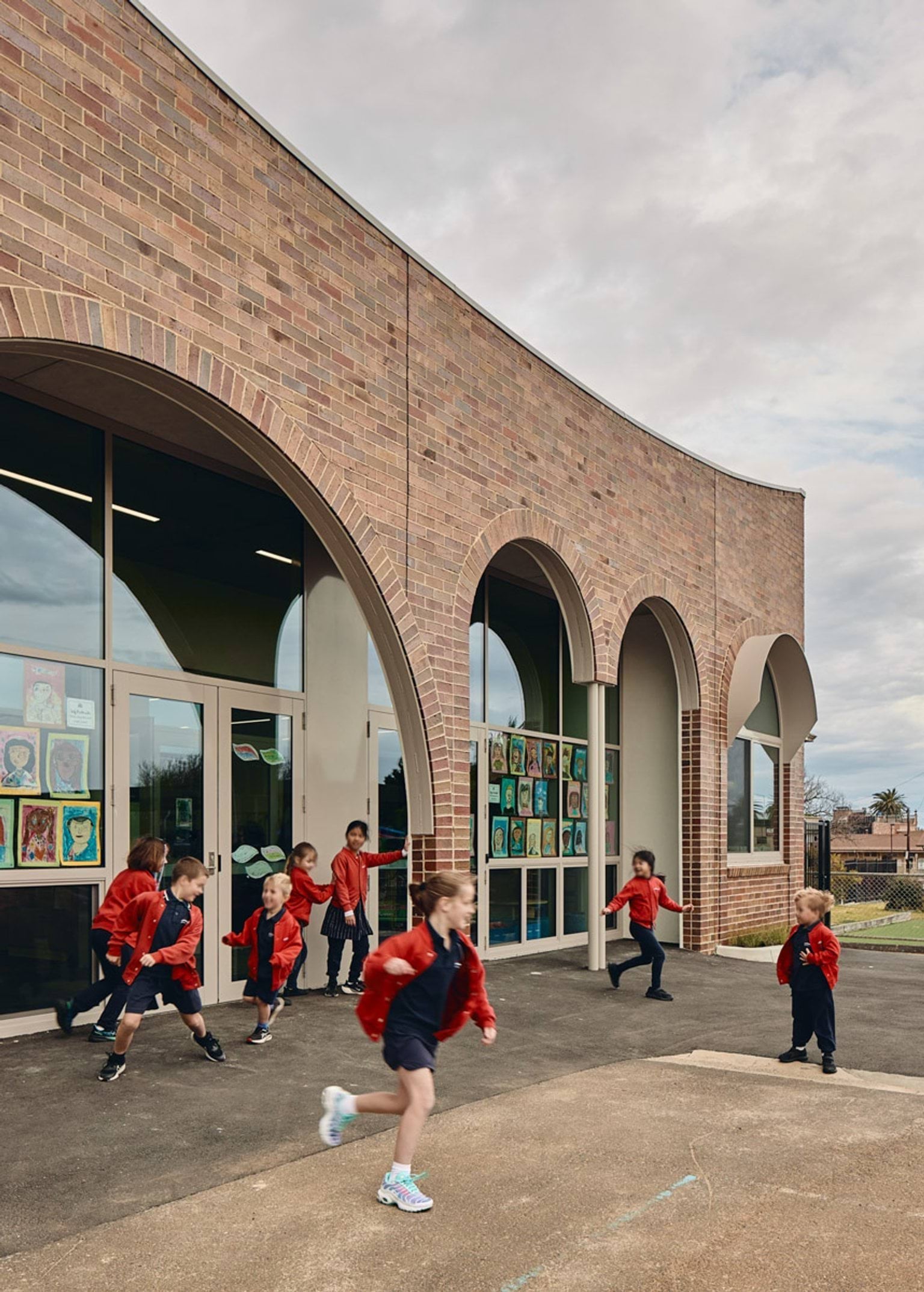 Close up of administration building. It is a brown brick building with arches above the windows and doors. There is a group of school students walking just outside the front door.