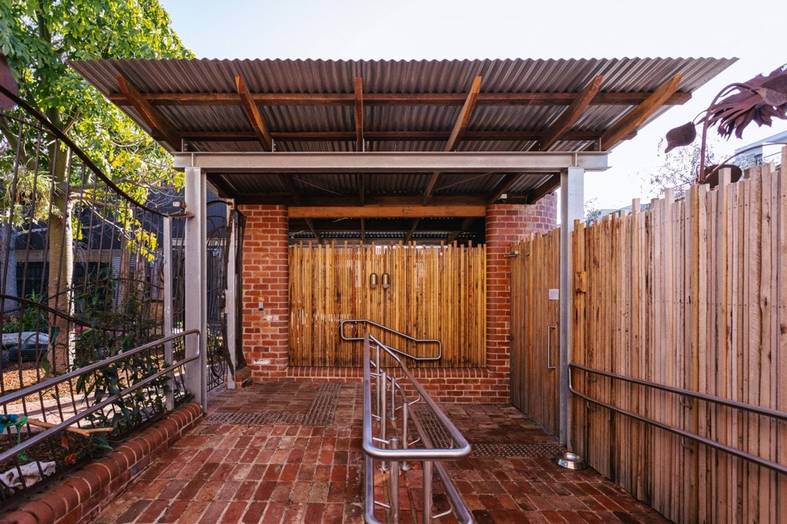 An outside entrance area of St Kilda & Balaclava Kindergarten. The ground is bricks, with a ramp and stairs. There is a covered roof. 