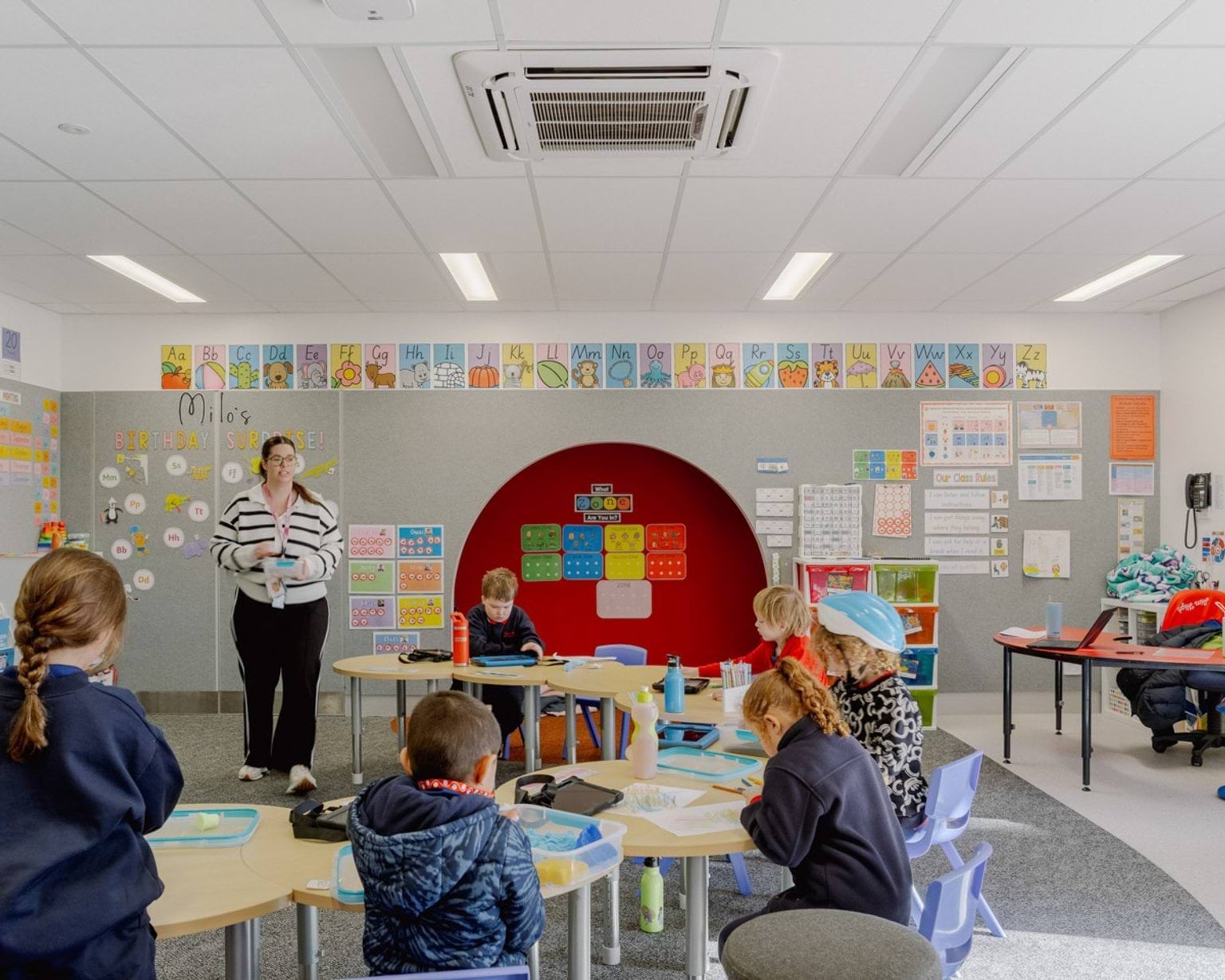 Inside a classroom of Swan Hill Specialist School with kids sitting at desks and a teacher standing. There are lots of colourful posters on the walls. 