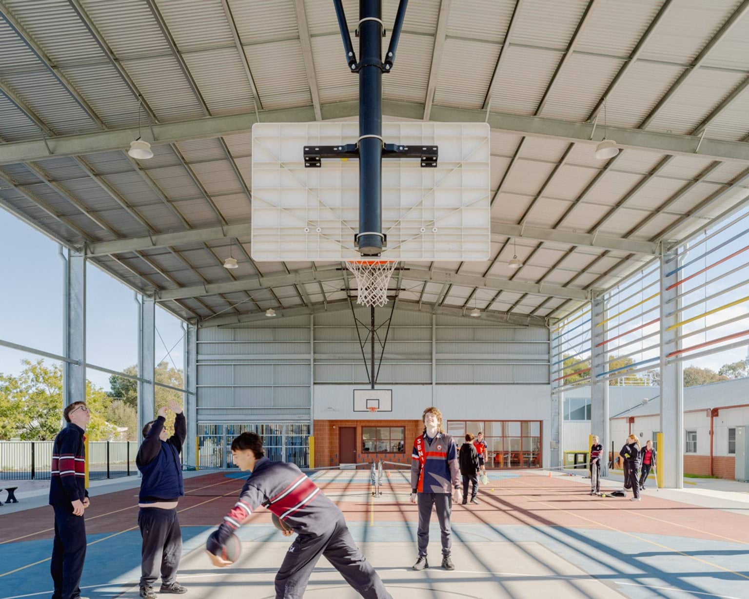 Another angle of the hard court inside the gymnaisum of Swan Hill Specialist School. There are students standing around playing basketball.