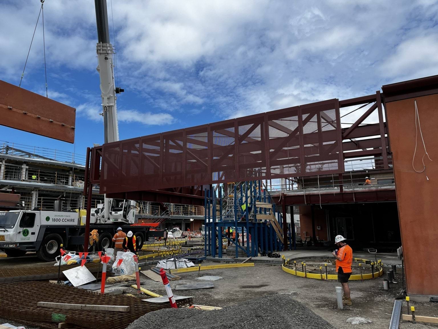 A crane shifting ochre red panelling to a metal mesh along the steel frame. 