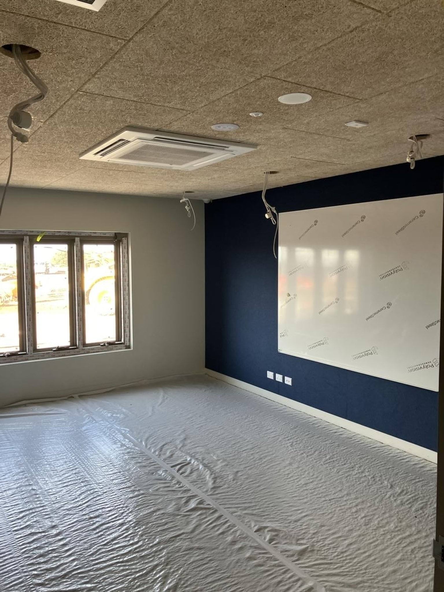 Interior of classroom with fibreboard ceiling and plastic membrane covering the flooring. Whiteboard covered with plastic coating. 