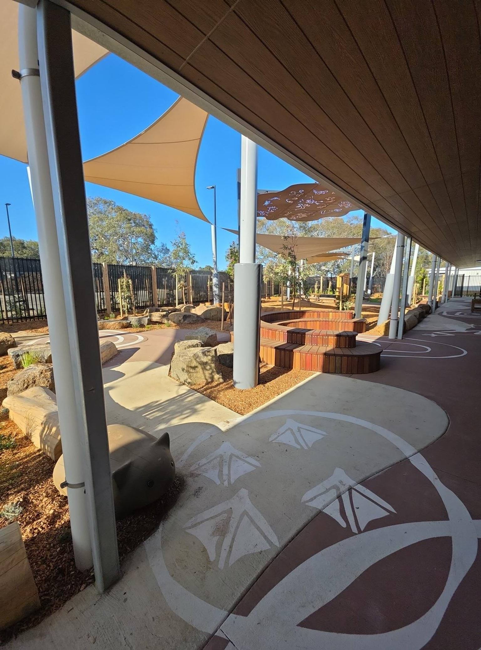 Biyala Primary School Kindergarten newly landscaped internal courtyard with First Nations influenced painted paths, shade cloth and metallic shading. Timber seating snakes through courtyard.
