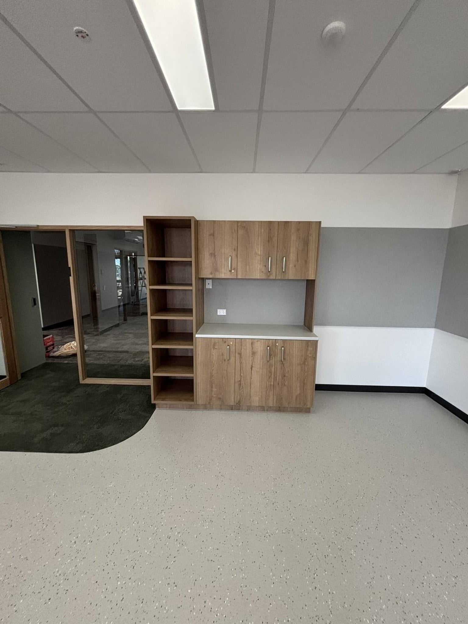 Inside the new Early Learning Victoria Numurkah (interim name) building, facing one of the walls that has a cupboard wall unit. Next to this is a doorway with a glass wall. 