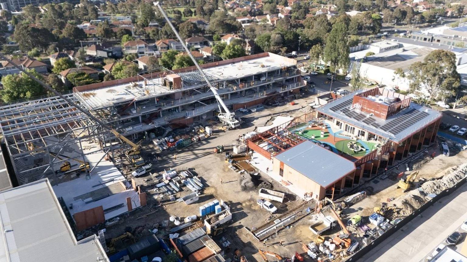 A high-angle photo of the Narrarrang Primary School construction site. The school buildings are at different stages of completed. There are 2 cranes on site and lots of other machinery, vehicles and construction materials. 