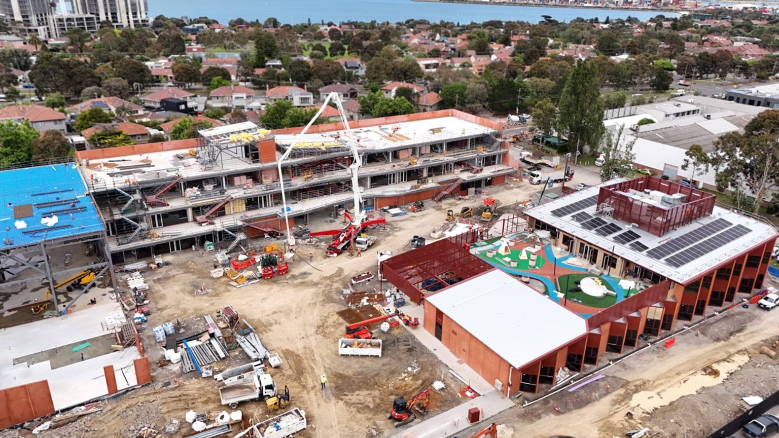 Overhead view of school site with buildings under construction. There are excavators and other construction vehicles on site.