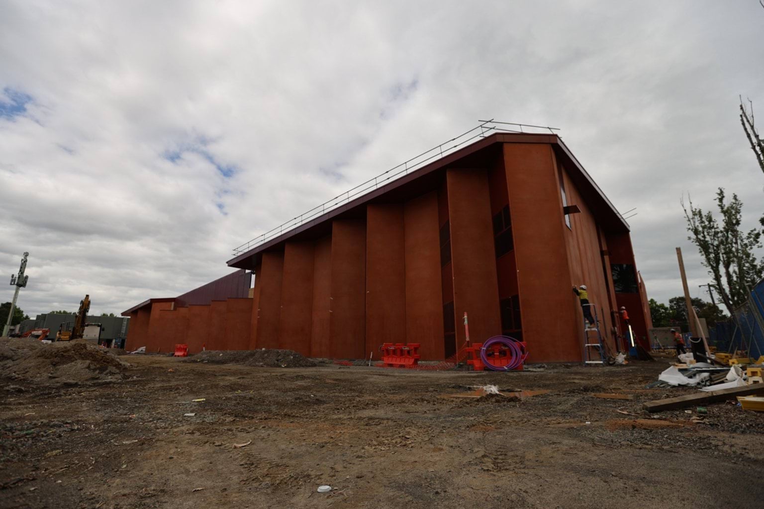 Multilevel school building under construction, as viewed from a low angle and zoomed out. It has orange walls and double doors with windows and scaffolding.