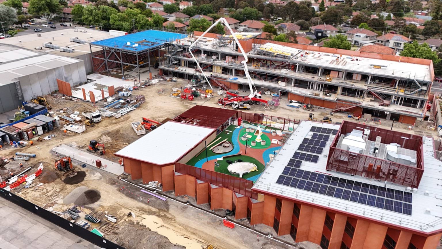 Overhead view of school site with buildings under construction. There are excavators and other construction vehicles on site.