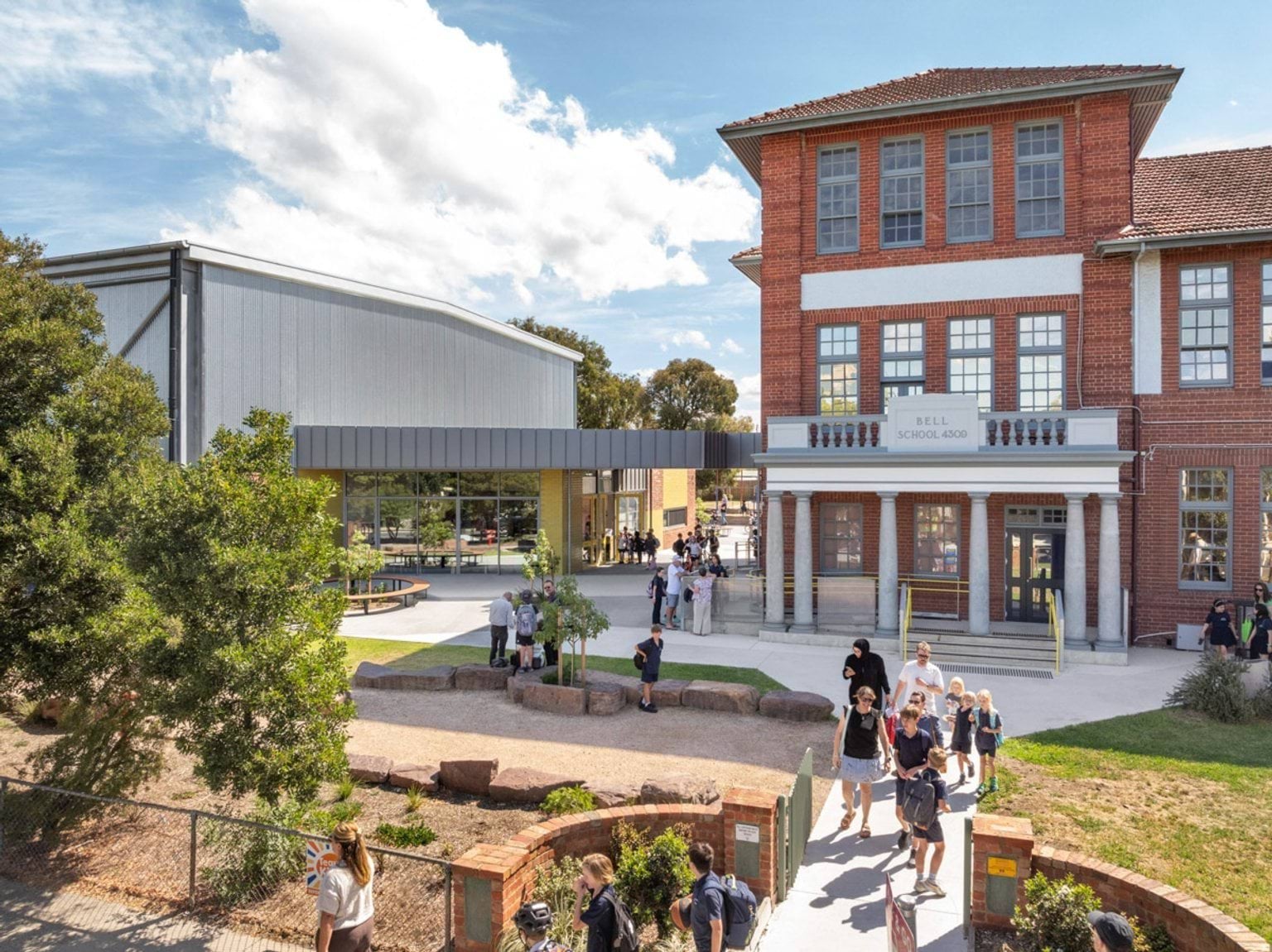 A heritage red brick school building with a tiled roof next to a modern sports hall with metal cladding and a covered walkway.