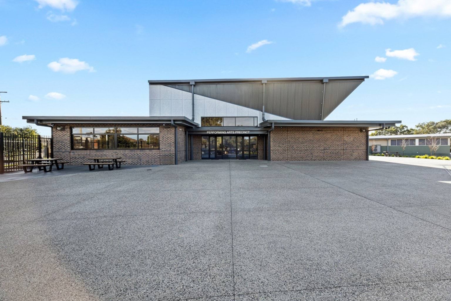 Wide front view of the Performing Arts Precinct with brick walls, large glass entry doors, and a distinctive angular roofline.