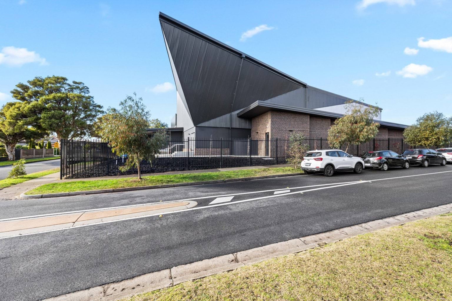 Street view of the Performing Arts Precinct showing its bold angular roof and brick walls, with cars parked along the roadside.