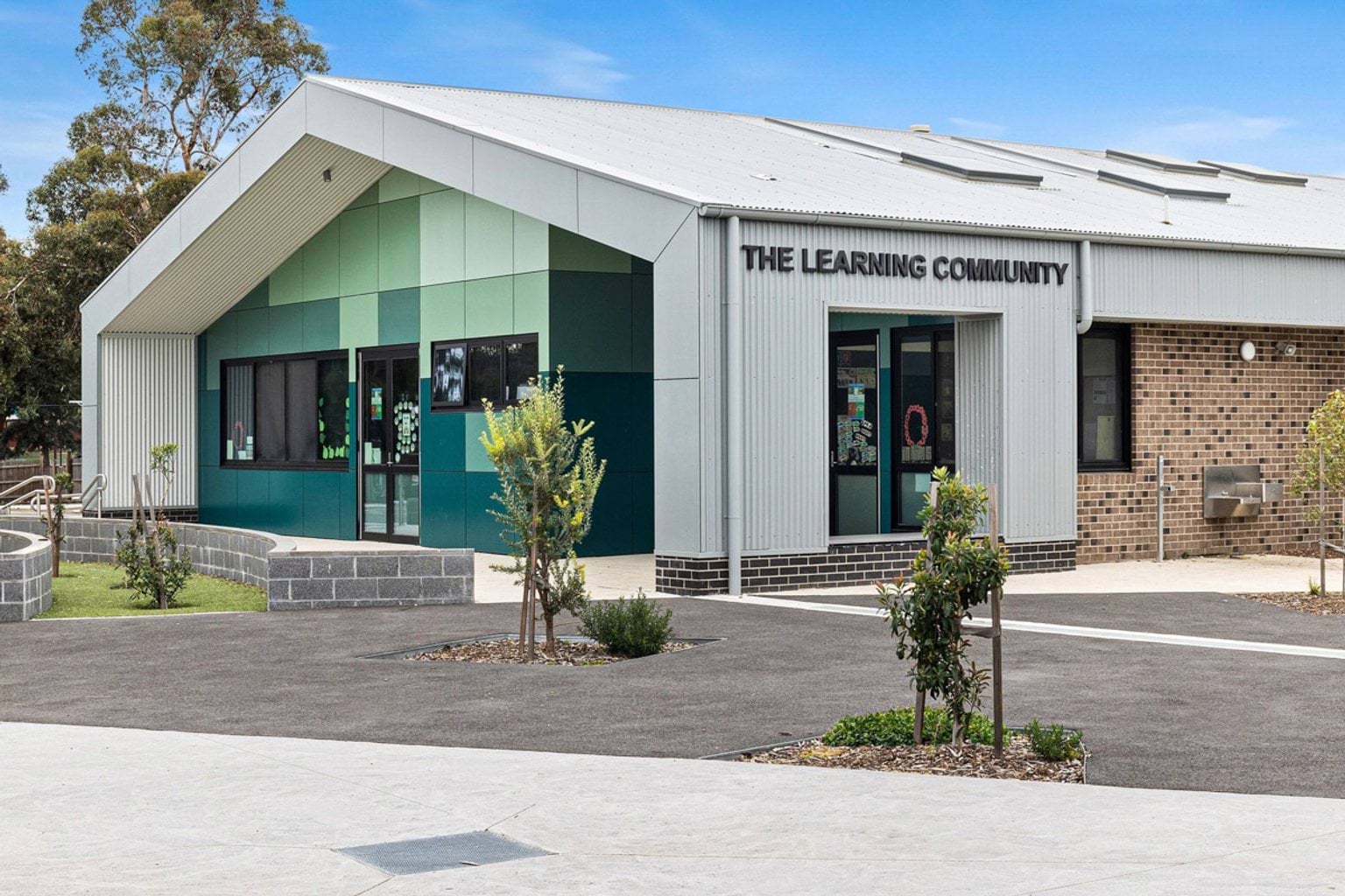 A modern school building with green cladding and a gabled roof. The sign reads “The Learning Community” above the entrance.