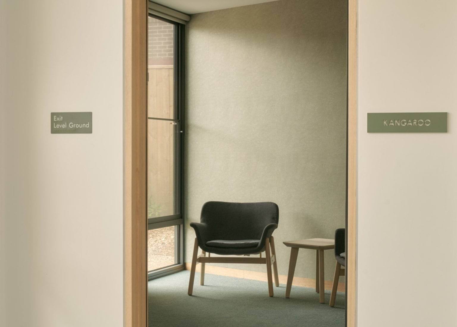 A small seating nook inside the kindergarten with a black armchair and side table near a full-height window.