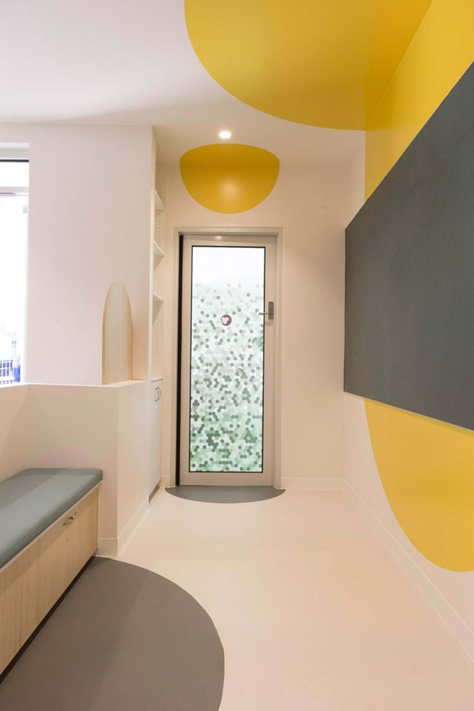 Small hallway with yellow circular wall and ceiling accents, grey feature panel and frosted glass door with geometric pattern