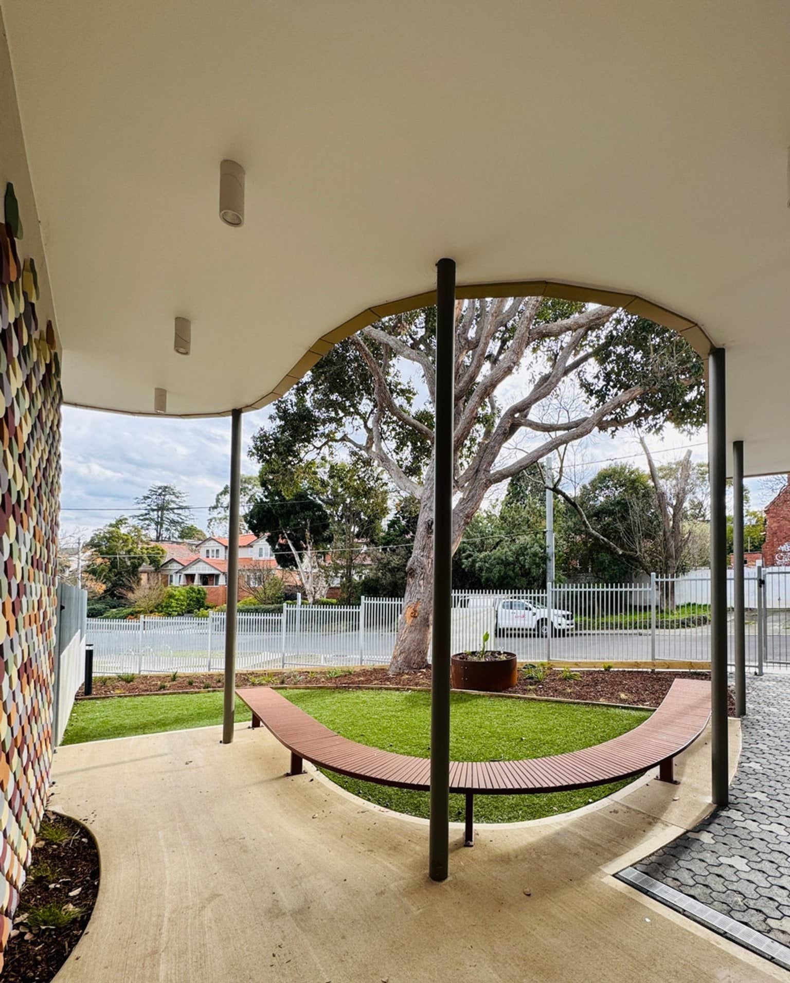 Covered outdoor area with curved roofline, timber bench seating and landscaped garden overlooking street