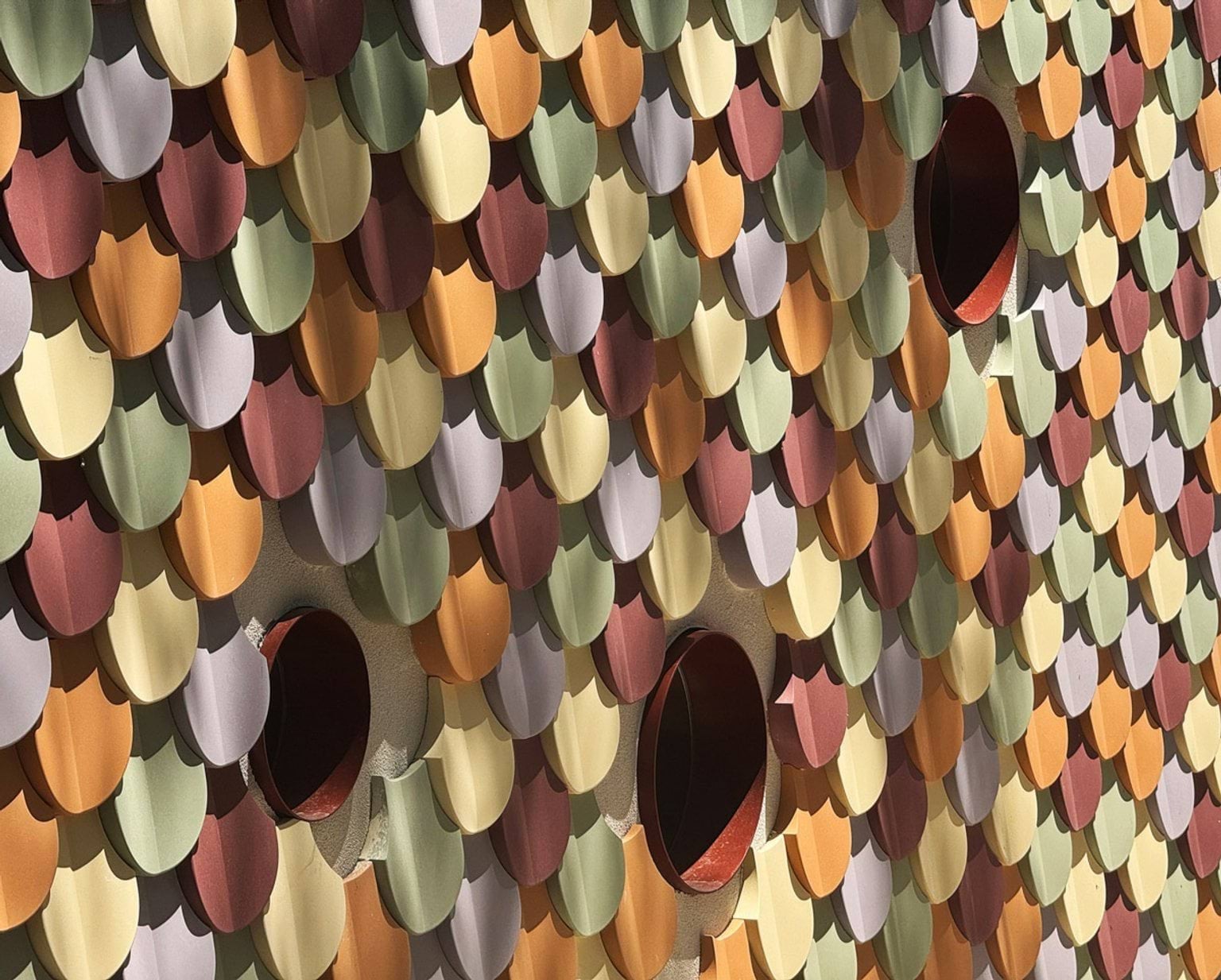 Close-up of colourful overlapping wall tiles in shades of orange, green, yellow and purple with circular windows