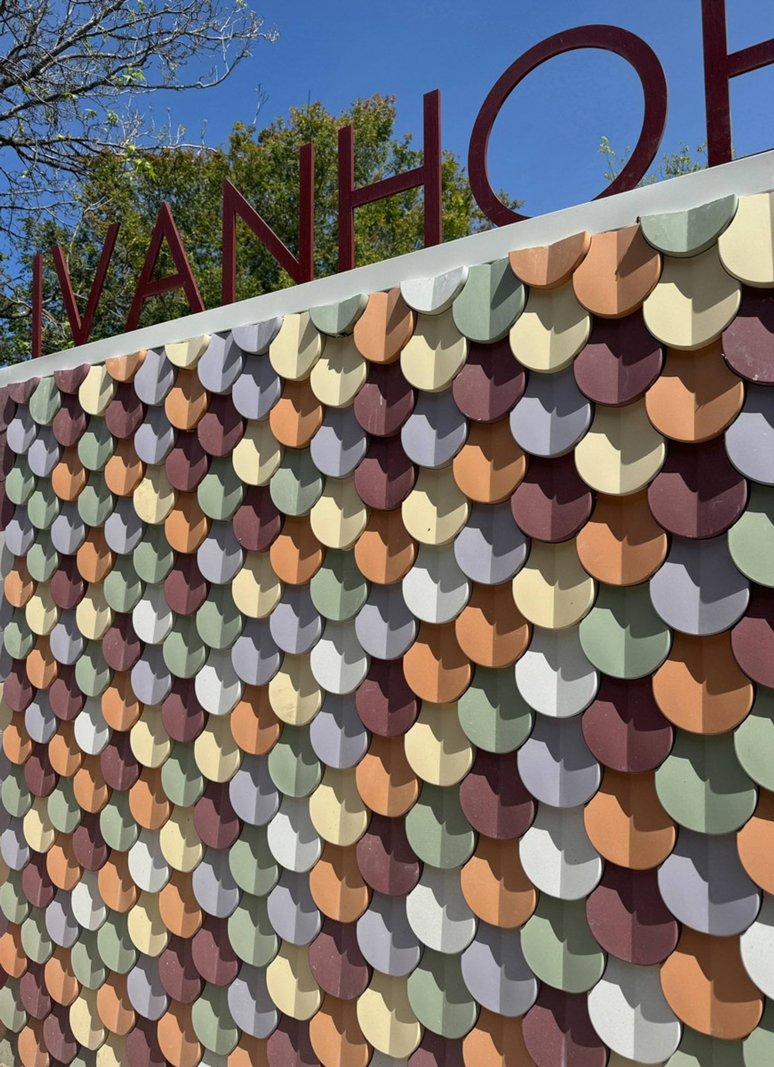 Entrance wall with multicoloured overlapping tiles and red metal letters spelling “IVANHOE” above