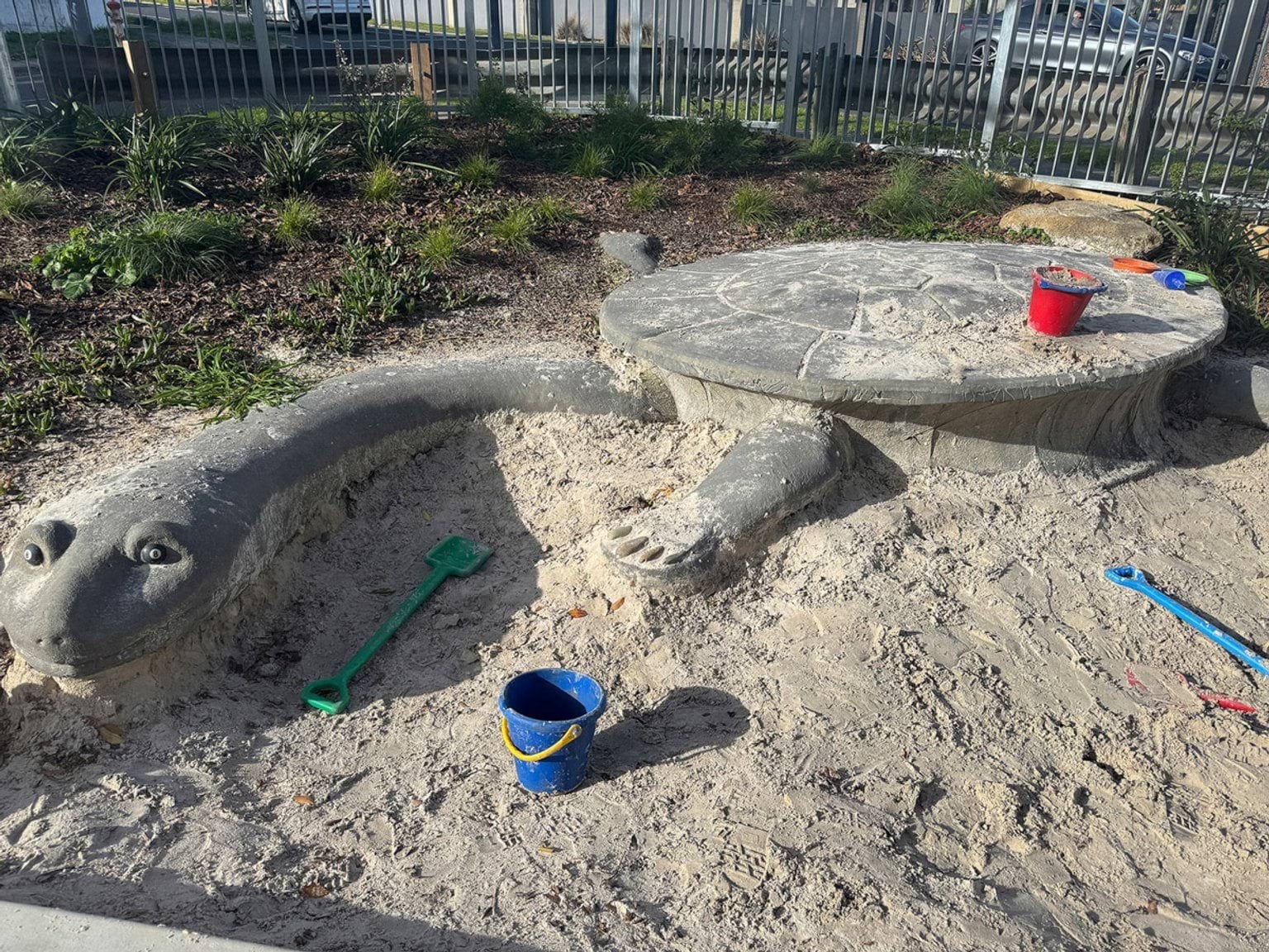 Sandpit featuring a sculpted turtle with buckets and spades scattered around in outdoor play space