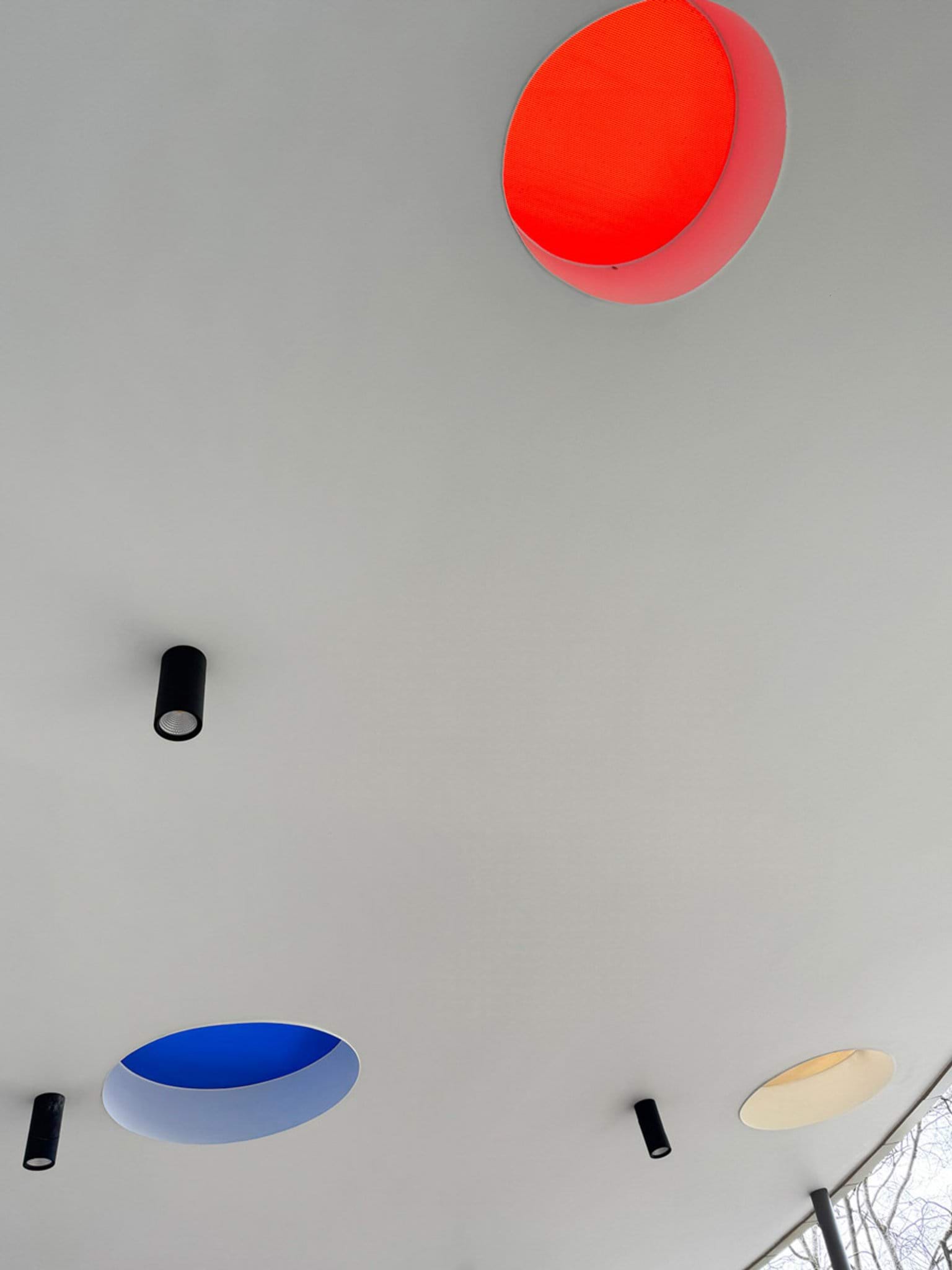 Ceiling with circular cut-outs in red, blue and yellow alongside black cylindrical light fittings