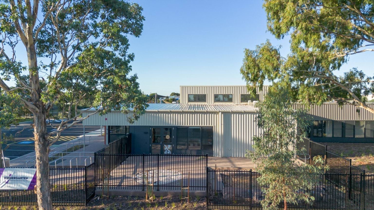 Exterior view of a modern building with metal cladding, large windows and fenced landscaped area