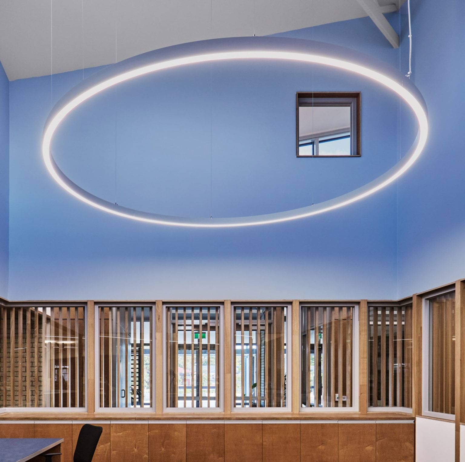 A blue feature wall with a large circular pendant light above. Timber slats and glass panels form the lower section of the wall.