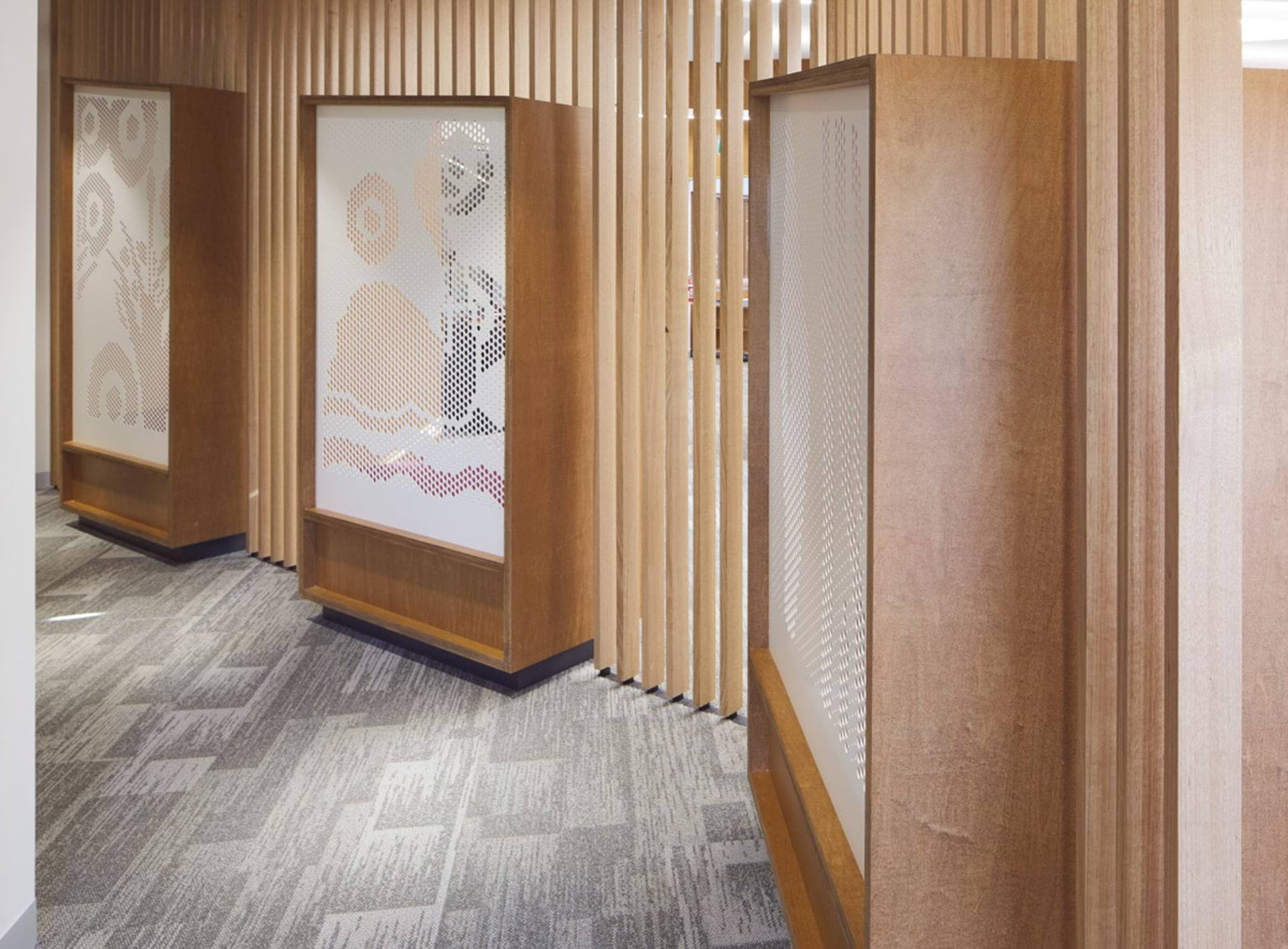 A hallway with timber slats and decorative panels featuring perforated designs. The floor is carpeted in a neutral tone.