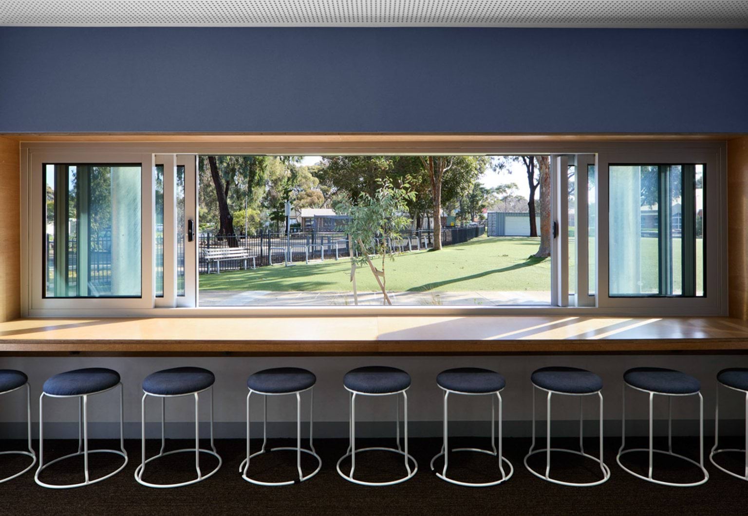 A long window bench with stools overlooking a grassy outdoor area and trees. The space has a blue feature wall.