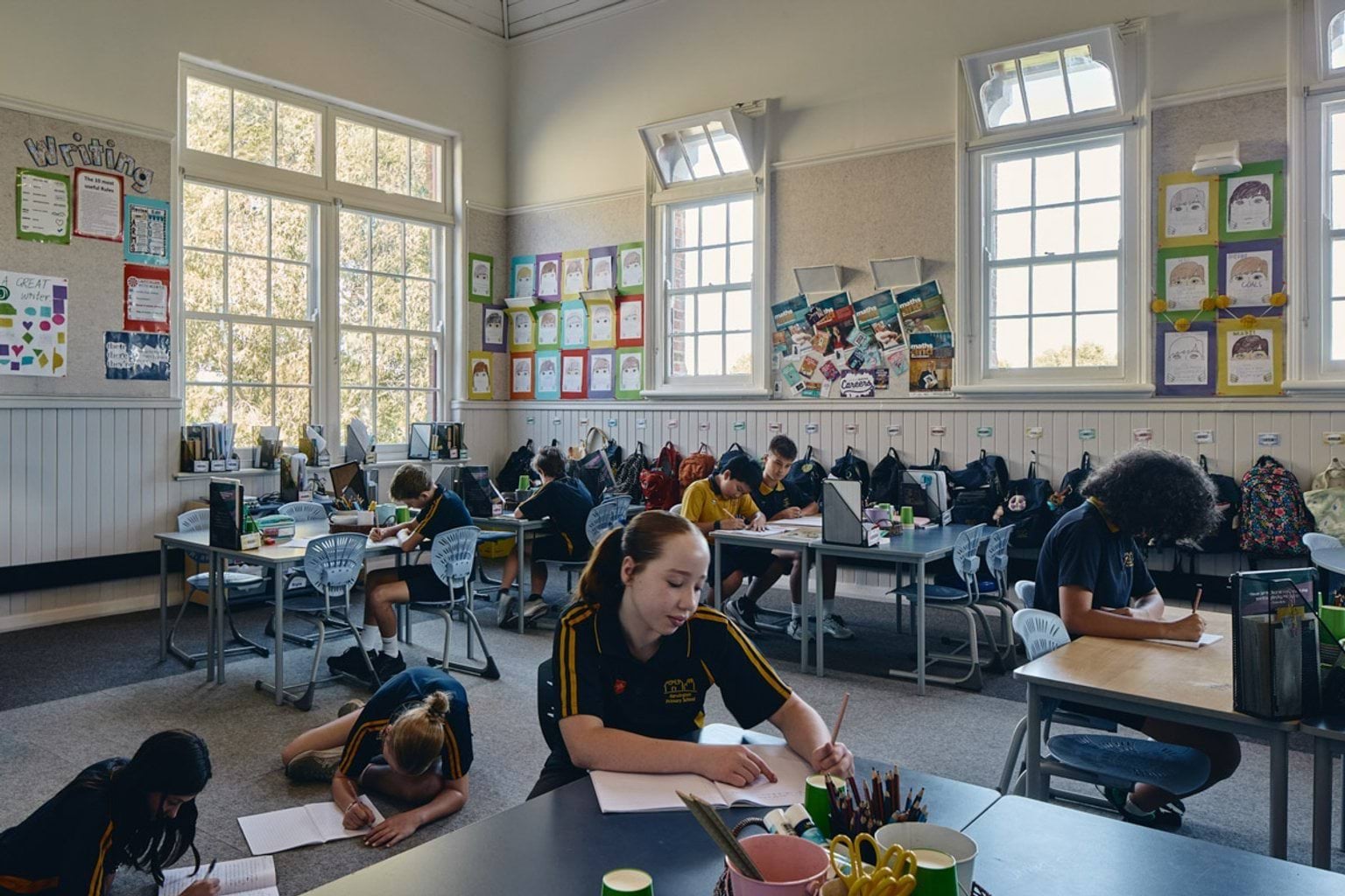 Classroom with students working at desks, colourful artwork displayed on walls and large windows overlooking trees
