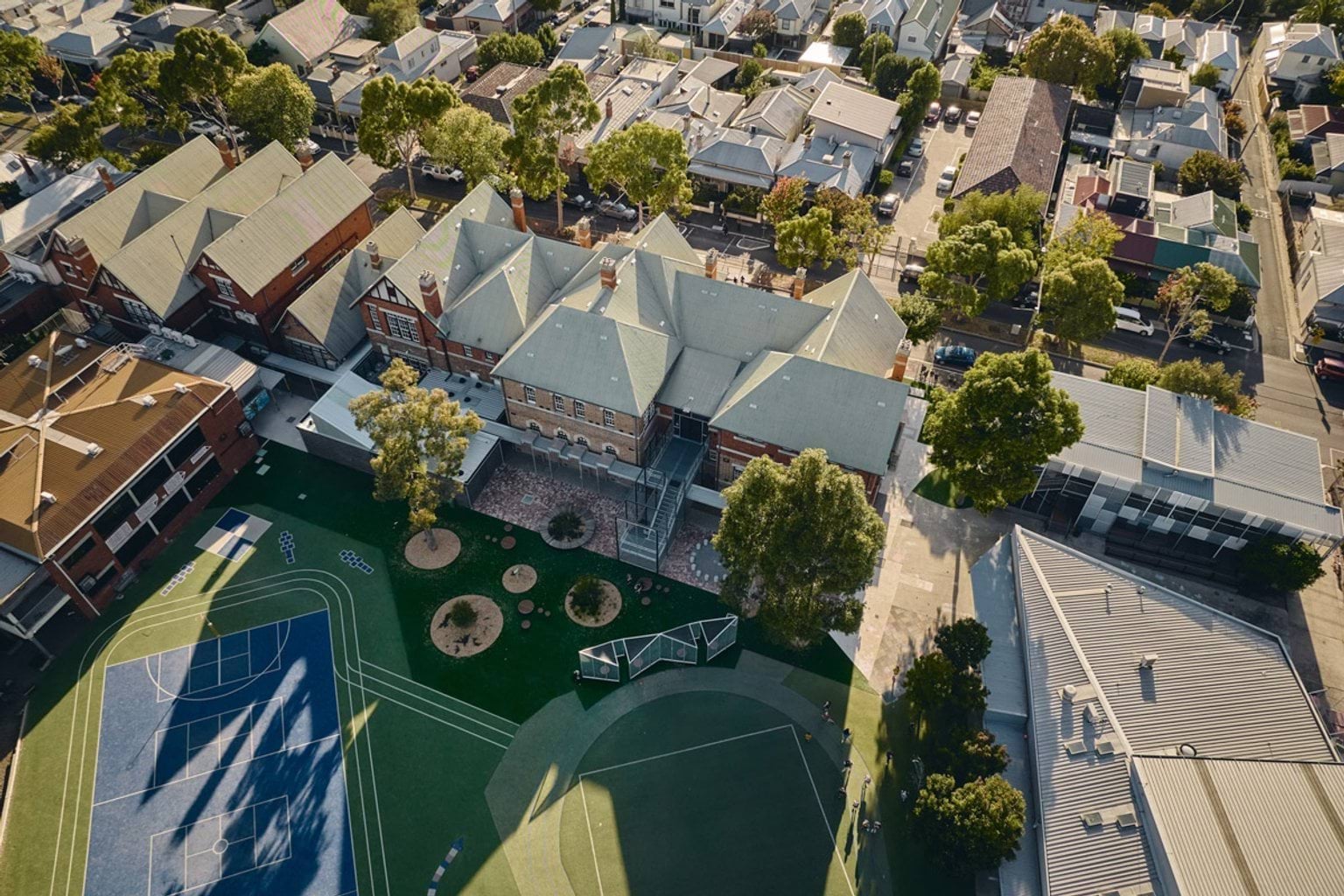 Aerial view of school buildings with pitched roofs, outdoor sports courts and surrounding residential streets