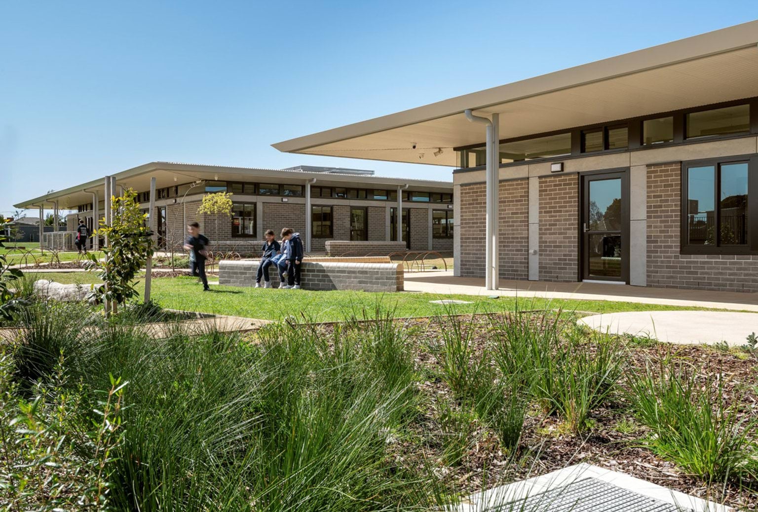 A landscaped courtyard with garden beds, young trees, and paved paths between modern brick school buildings