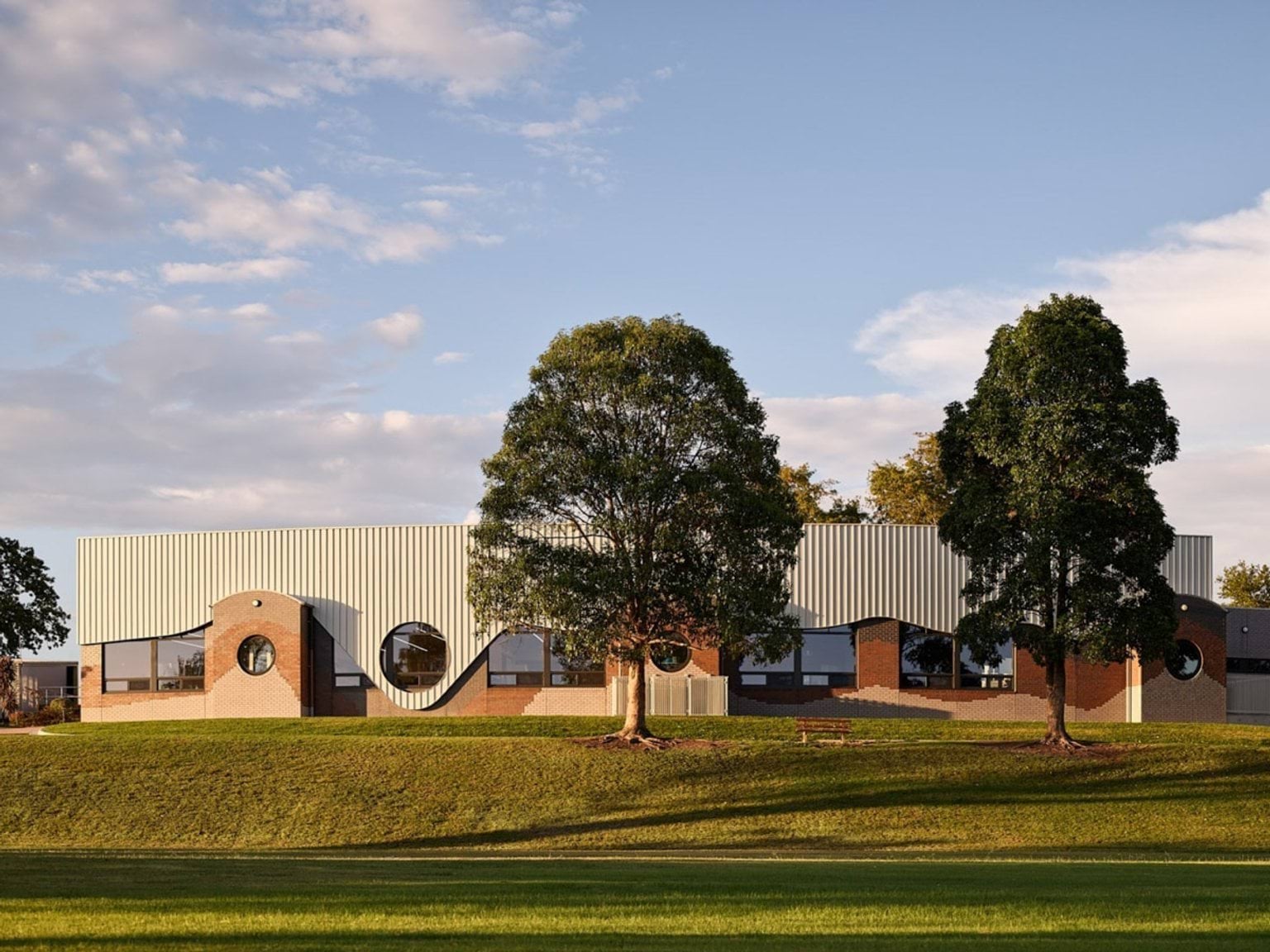 Front elevation of school building featuring curved metal cladding and circular windows, with trees in foreground