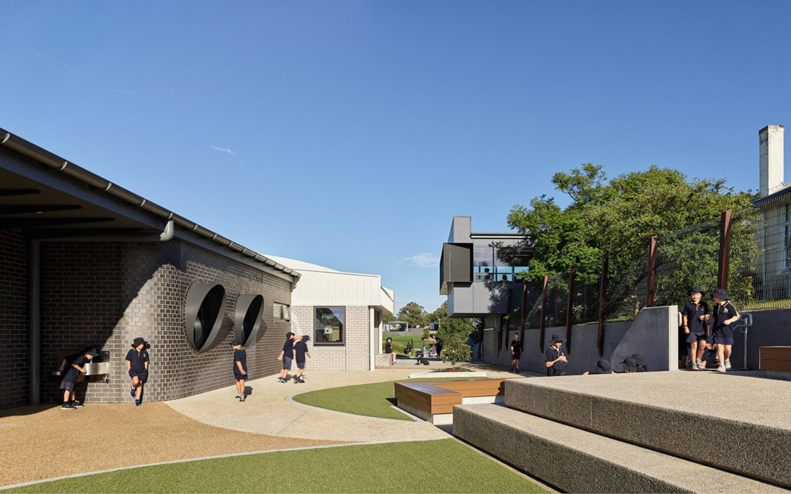 Courtyard with tiered seating and landscaped play area between contemporary school buildings, students playing and talking