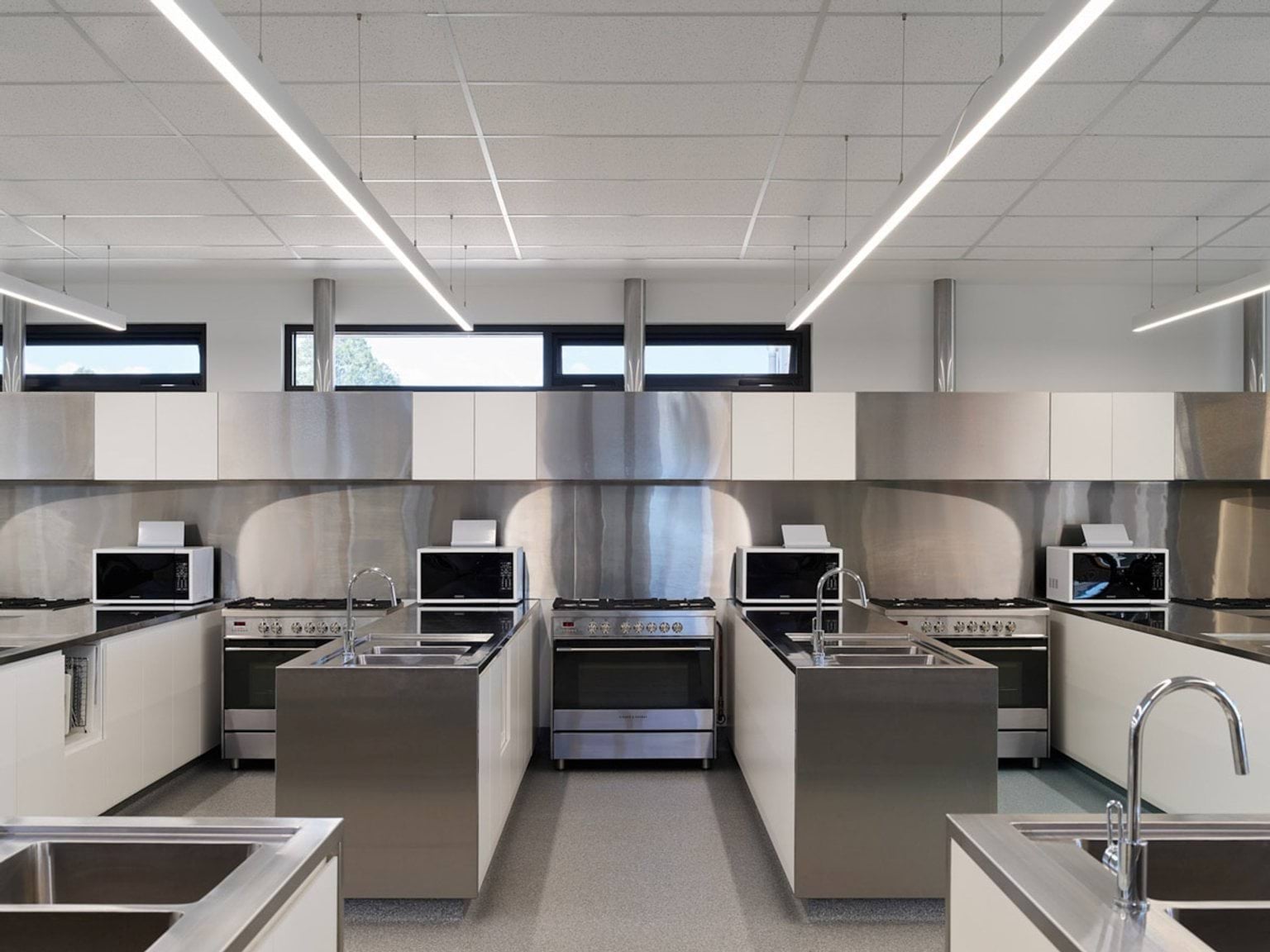 Kitchen classroom with stainless steel benches, ovens, microwaves and sinks arranged in rows