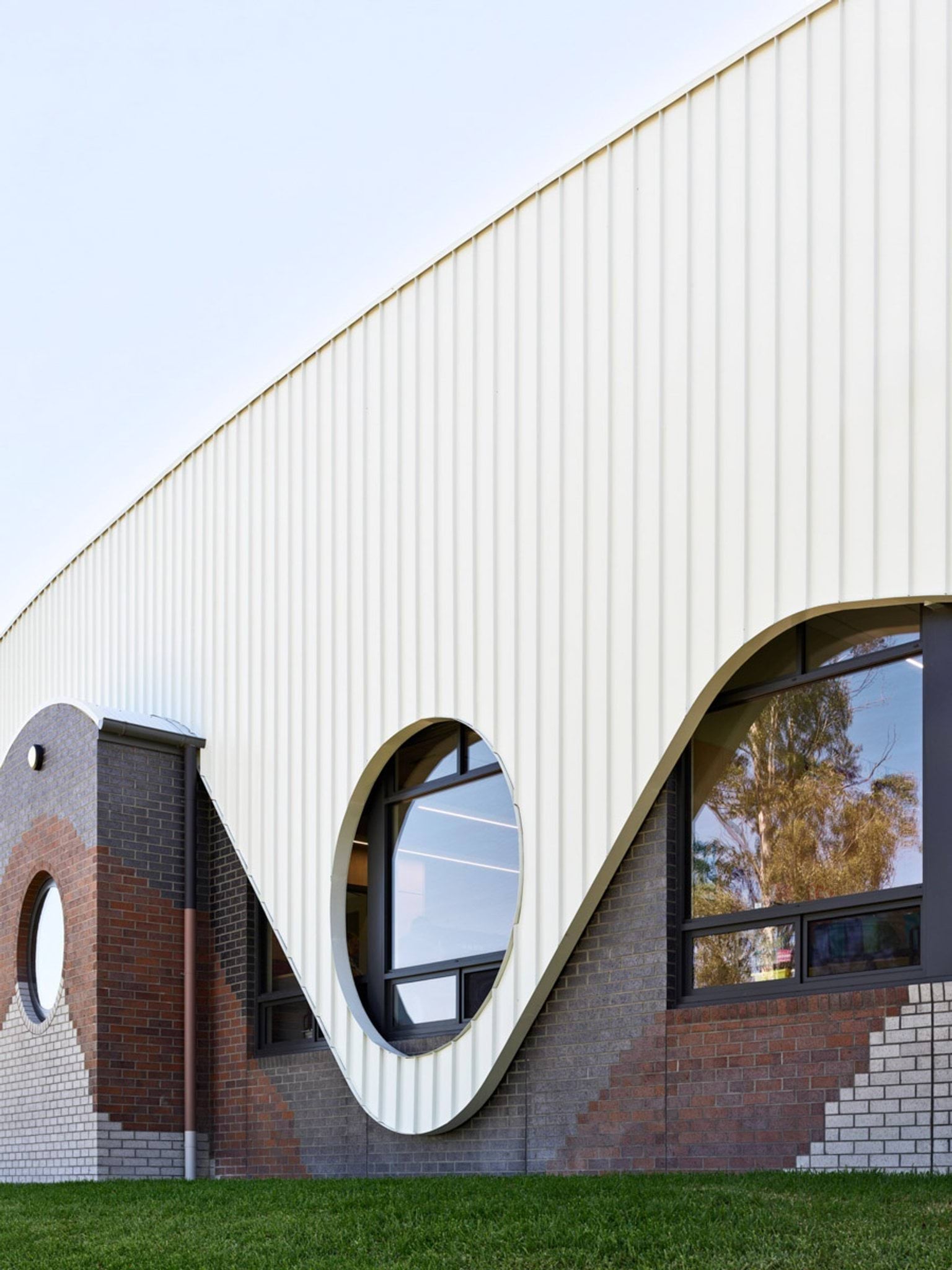 Close-up of school building facade with curved metal cladding and circular feature window above brickwork