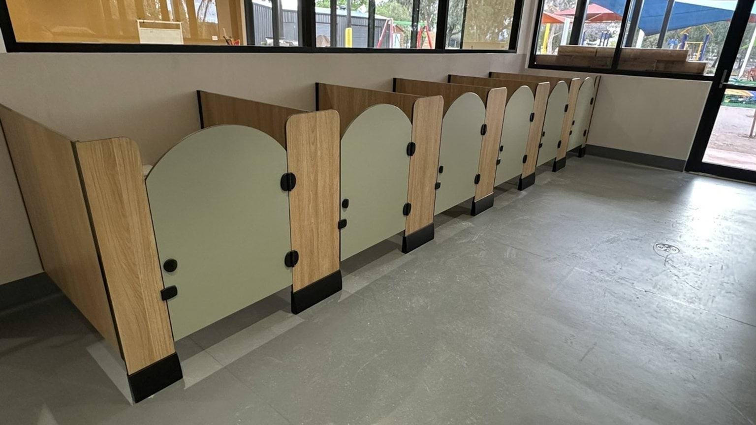 A row of small timber cubicles with curved doors inside the kindergarten, likely for storage or personal spaces. Large windows overlook the outdoor play area.