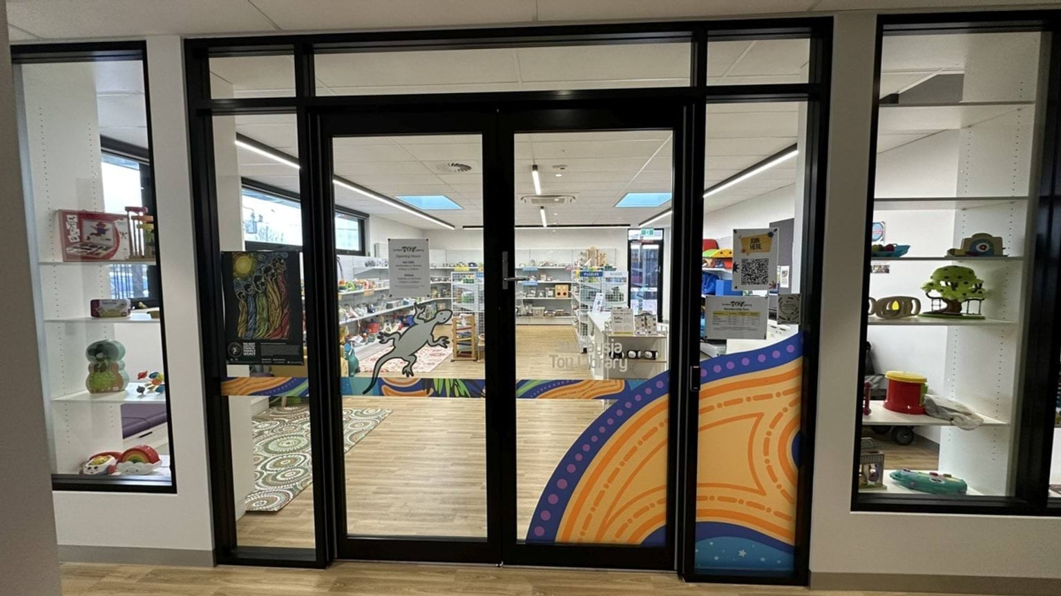 Glass doors leading to the toy library, decorated with artwork. Inside, shelves are filled with toys and educational resources.