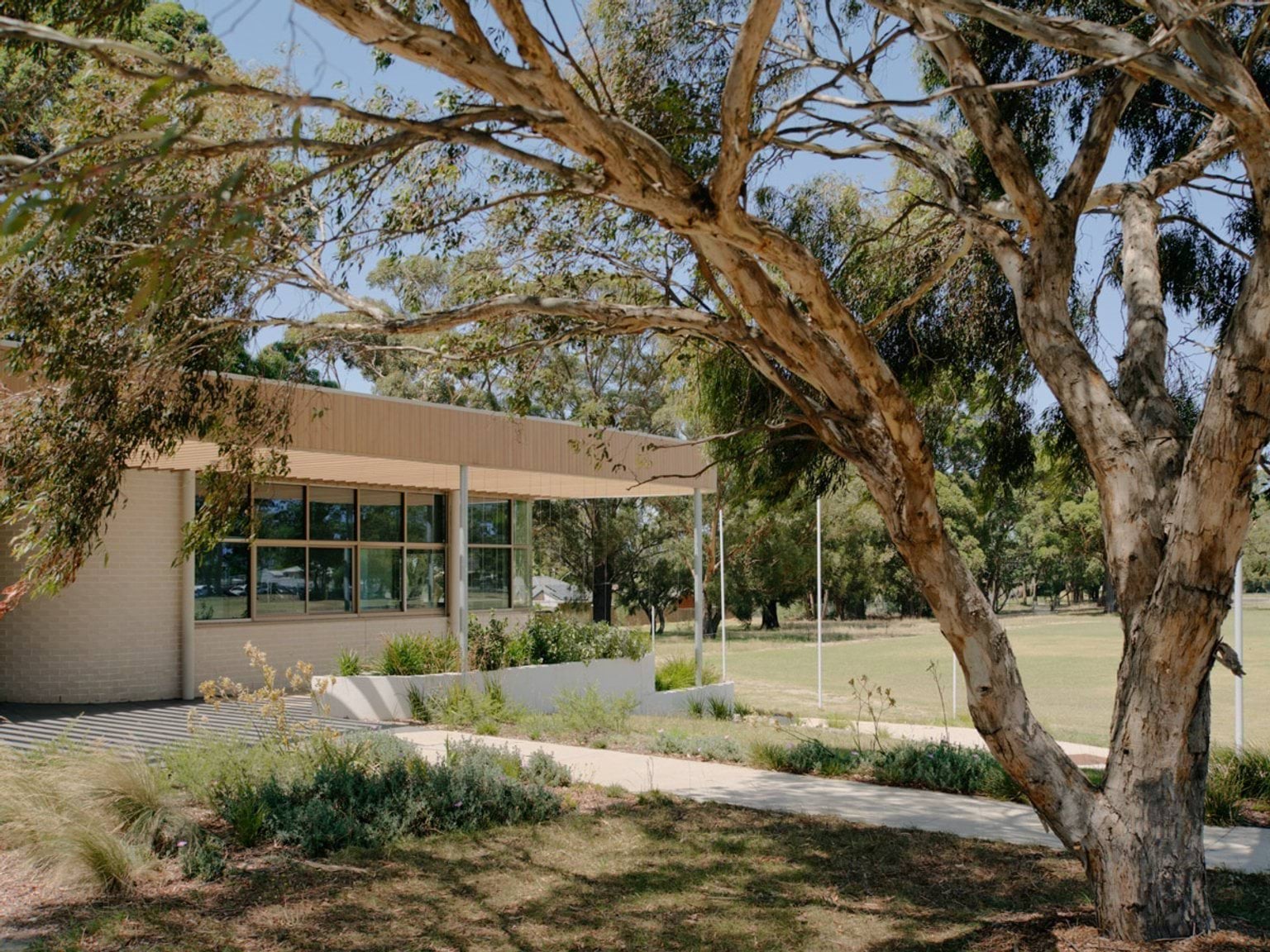 Side view of the centre with a timber facade, large windows, and landscaped garden beds. A concrete path runs alongside the building under mature trees.